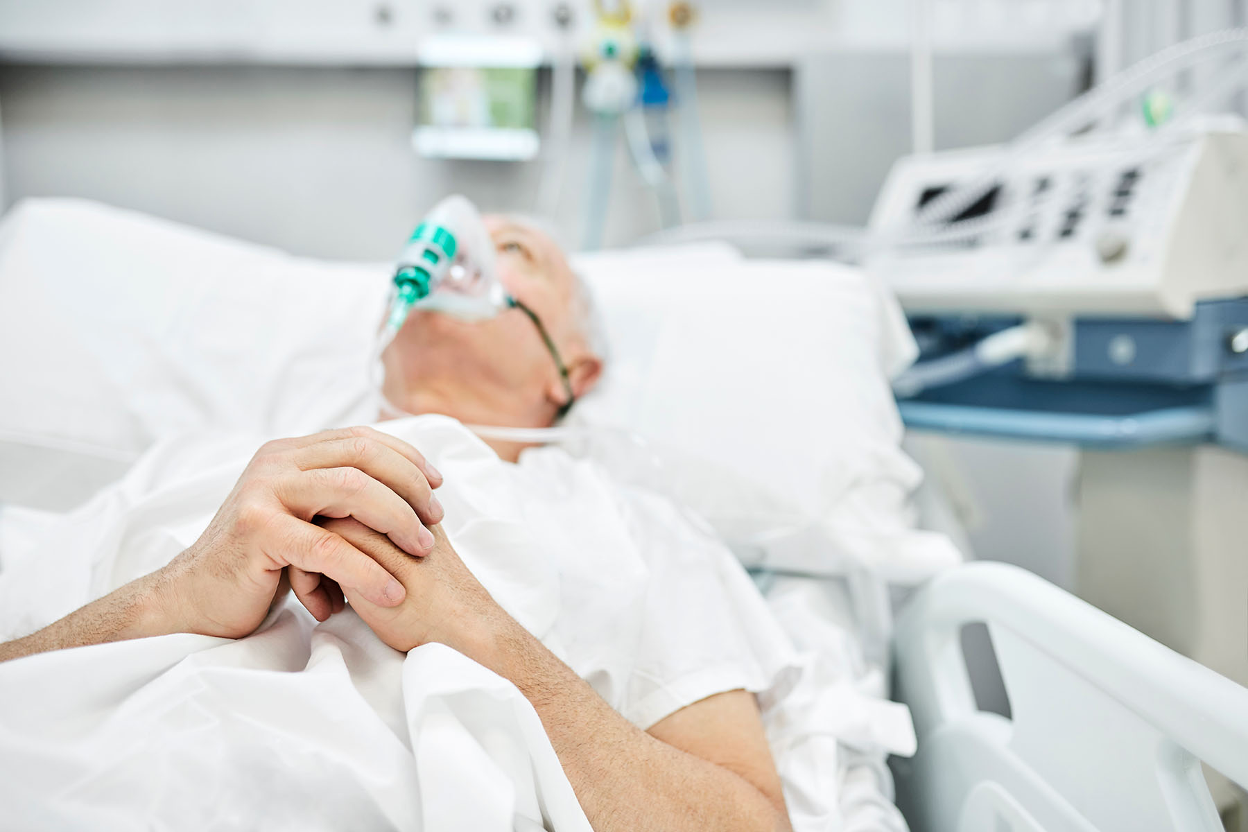 Elderly man lying on hospital bed with oxygen mask on